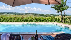 Ein Poolbereich mit Blick auf Weinberge, ein Tisch mit Flasche und Gläsern sowie zwei Stühle.