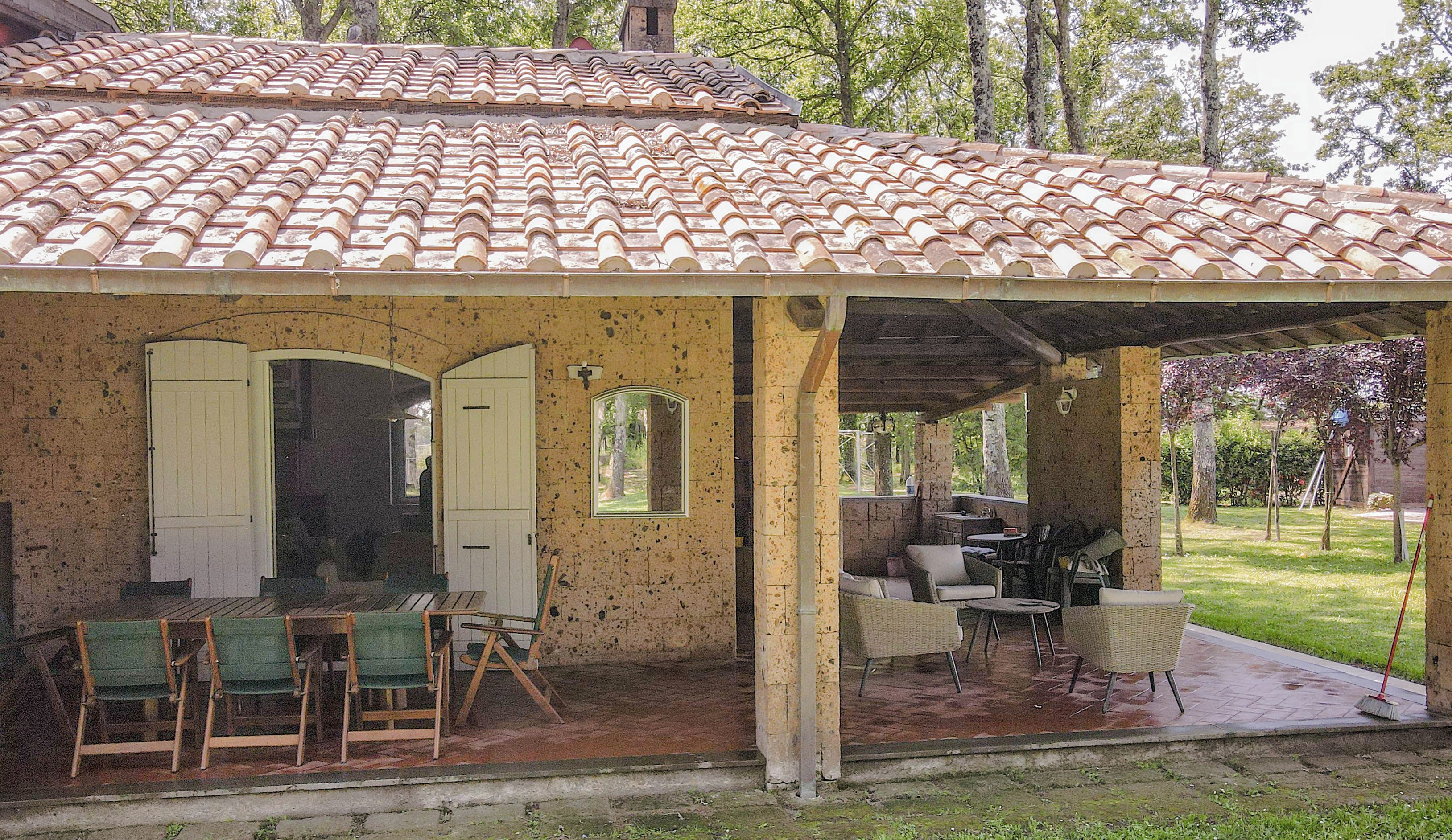 A covered outdoor seating area with a tiled roof, a brick wall, and a view of the surrounding trees.