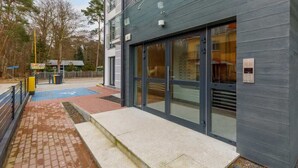 A modern building with large glass doors, a brick pathway, and a small outdoor area with a blue mat.