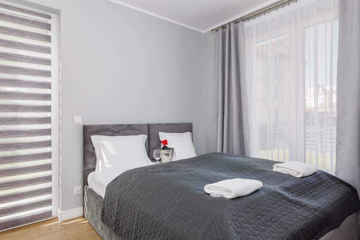 Une chambre d’hôtel avec un grand lit, une table de chevet avec un verre, et une vue à travers des rideaux transparents.
