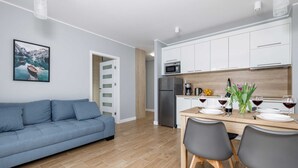 A modern kitchen with white cabinets, a dining table with chairs, and a blue sofa.
