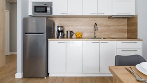 A modern kitchen with white cabinets, a stainless steel refrigerator, a microwave, a coffee maker, and a sink.