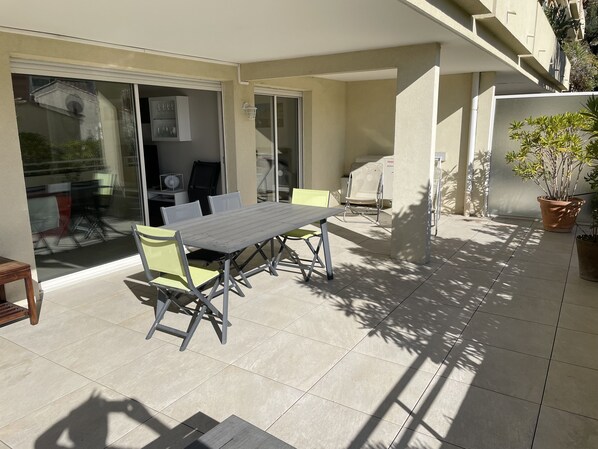 An outdoor patio with a table and chairs, a sliding glass door, and a potted plant. - CAVALAIRE: The Sun of Your Vacation!<br>—a comfortable apartment just 8 minutes from the beach (Cavalaire-sur-Mer)