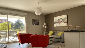 Un salon moderne avec un canapé gris, des fauteuils rouges, une table à manger et un îlot de cuisine.