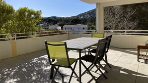 Un balcon avec une table et des chaises, donnant sur un paysage vallonné parsemé de maisons.