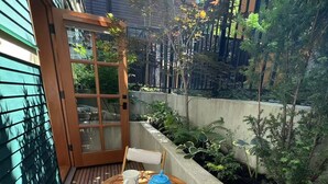 Une terrasse en bois avec une table ronde et deux chaises, une petite table blanche et une théière bleue.