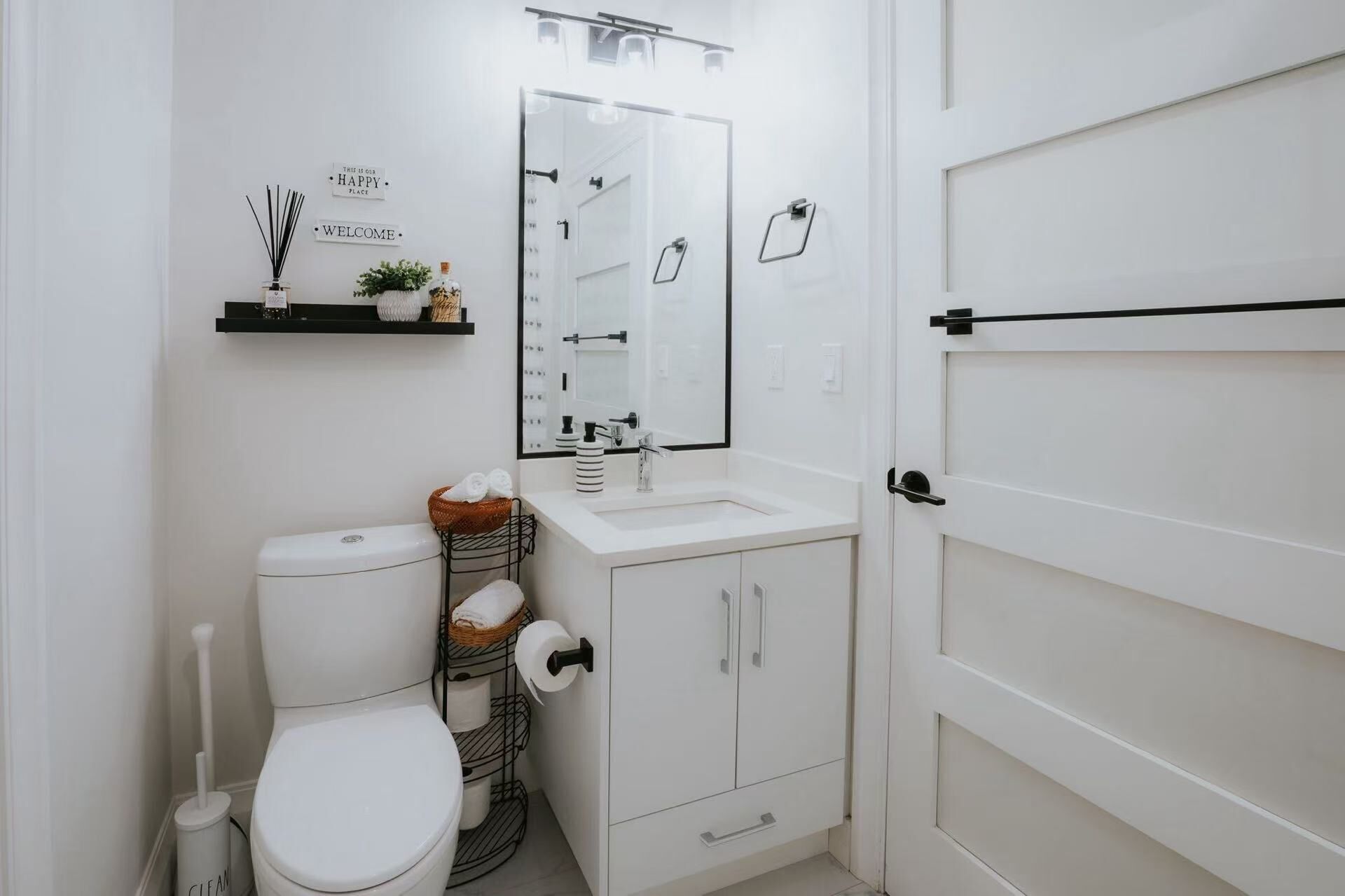 Une salle de bain moderne équipée de toilettes, d’un lavabo et d’un miroir. On y trouve des étagères avec des articles de toilette et un porte-serviettes.