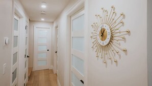 Un couloir avec des portes blanches, une horloge fixée au mur et des luminaires encastrés.