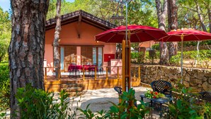 A rustic building with a wooden deck, outdoor seating, and red umbrellas.