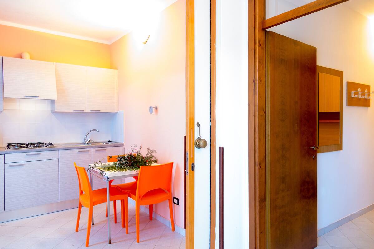 Una cocina moderna con armarios blancos, una estufa a gas y una mesa de comedor con sillas naranjas.