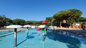 A swimming pool with clear blue water, surrounded by a white fence, and shaded by umbrellas.