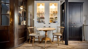 Een eetgedeelte met een ronde houten tafel en twee stoelen, een kast met glazen deuren en een donkere deur op de achtergrond.