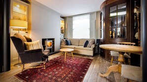 Een gezellige woonkamer met een open haard, een bank, een stoel, een klein rond tafeltje en een kamerkleed met een patroon.