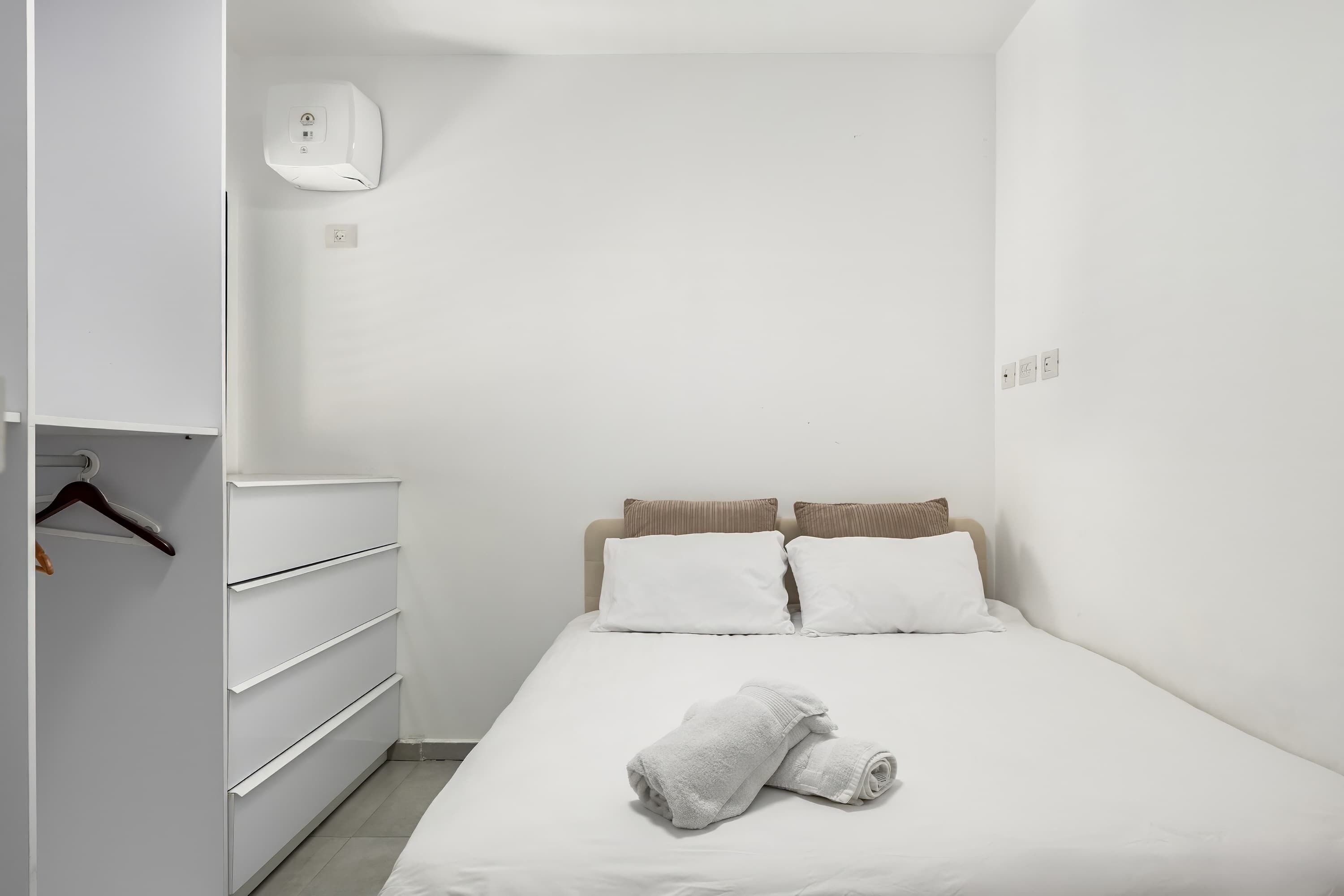 Ein schlicht eingerichtetes Schlafzimmer mit Bett, weißer Bettwäsche und einem weißen Kleiderschrank.