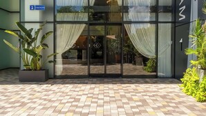 L'ingresso di un edificio con porte in vetro, una pianta in vaso e un pavimento piastrellato.