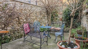 A stone wall, metal chairs, a table, and potted plants in a courtyard. - Naunton Cottage (Lyme Regis)