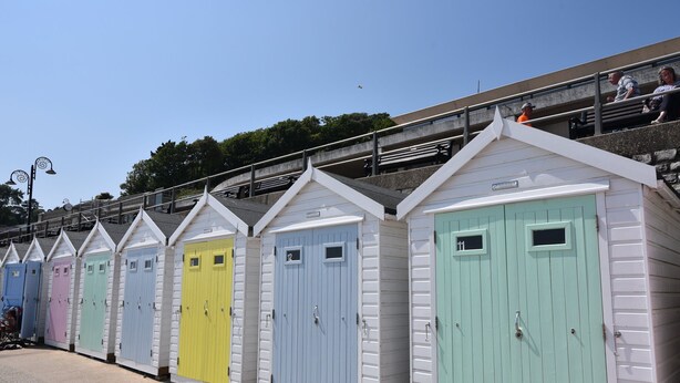 A row of colorful beach huts with numbered doors, a staircase leading to a viewing platform, and a clear sky. - Naunton Cottage (Lyme Regis)