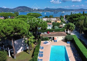 A resort with a swimming pool, lounge chairs, and a view of the sea and boats.