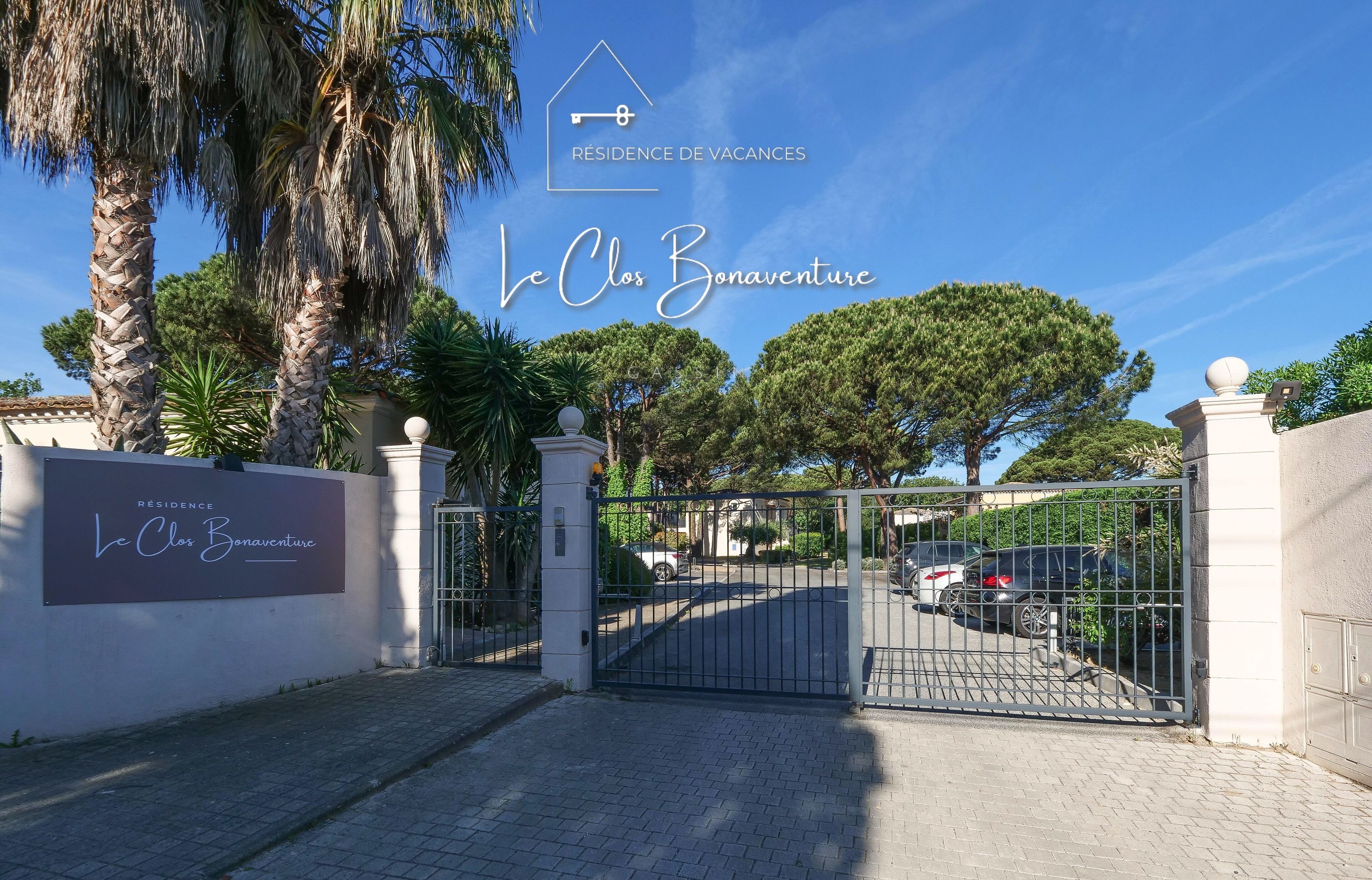 A gated entrance to Le Clos Bonaventure, a vacation residence with a clear sky and palm trees.