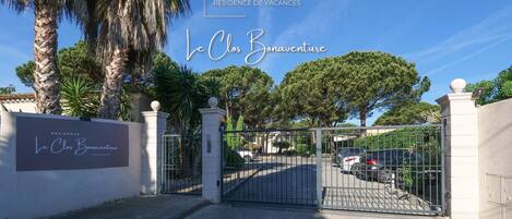 A gated entrance to Le Clos Bonaventure, a vacation residence with a clear sky and palm trees.