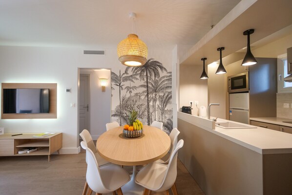 A modern kitchen with a central island, a dining area with a round table and white chairs, and a wall-mounted TV.