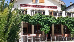 Un edificio con el letrero "LE 1050 RESTAURANT HOTEL SAINT-AGRÈVE", con terraza y fachada cubierta de hiedra.