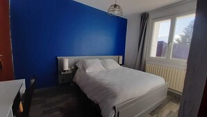 Un dormitorio con cama, mesita de noche, lámpara, ventana y vistas al exterior.