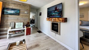A living room with a wooden floor, a fireplace, a mounted TV, and a ceiling light fixture.