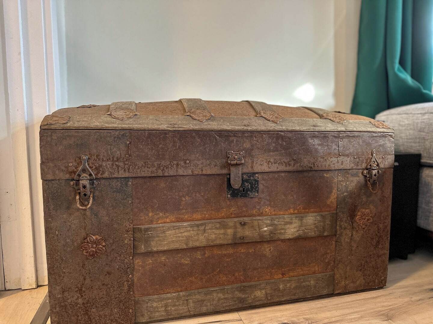 A vintage wooden trunk with metal latches and decorative carvings, placed on a wooden floor.