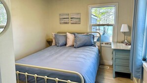A bedroom with a bed, a desk, a lamp, and a window with a view of trees.
