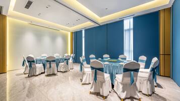 Un salón de conferencias con mesas redondas, sillas blancas con cintas azules y una pared de acento en tono azul.