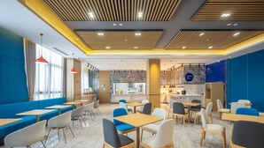 Un café moderne avec des sièges bleus, des tables en bois et un espace cuisine à l’arrière-plan.