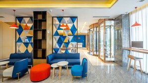 Un hall d’entrée moderne avec des canapés bleus, des poufs rouges et une cloison en verre ornée de motifs géométriques.