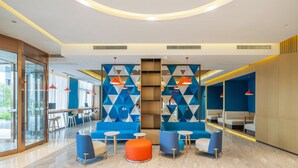 Un hall d'entrée moderne avec des sièges bleus, une colonne centrale en bois et des luminaires suspendus rouges.