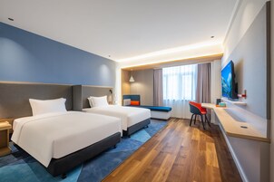 Habitación de hotel con dos camas, un escritorio, un televisor y una ventana con cortinas.