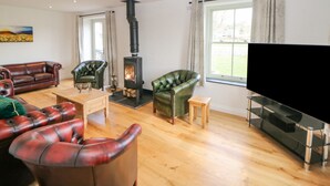 A living room with a fireplace, leather sofas, a television, and a large window. - Dove Meadows House (Buxton)