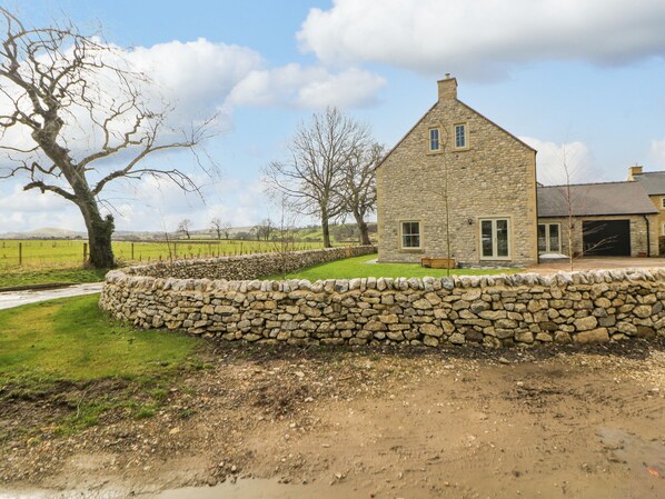 A stone house with a stone wall in front, a grassy yard, and a tree.