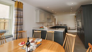 A modern kitchen with a dining area, featuring a wooden table, chairs, and a bottle of wine. - Dove Meadows House (Buxton)