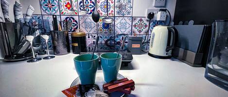 A kitchen with a tiled backsplash, a coffee maker, a kettle, and two blue cups on the counter.