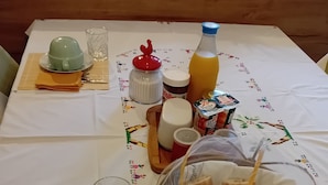 Ein Frühstücksangebot mit Teekanne, Tassen, einem Glas, einer Orangensaftflasche, einem Nutella-Glas, einem Brotkorb und einem kleinen Glas.