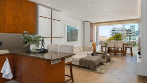 A modern kitchen with wooden cabinets, a central island, and a dining area with a table and chairs. - Seacliffe 307 (Cape Town)