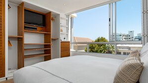 A bedroom with a large bed, wooden closet, and a TV. - Seacliffe 307 (Cape Town)