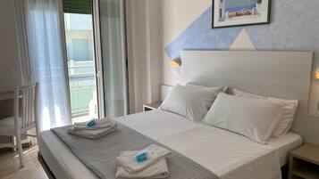 A hotel room with a bed, a nightstand, a picture on the wall, and a window with curtains.