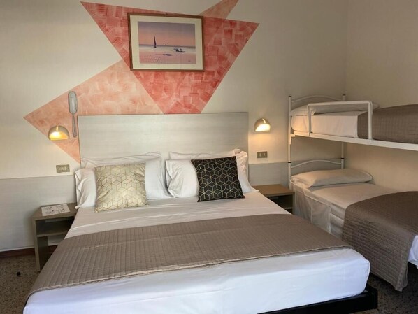 Een hotelkamer met een groot bed, twee nachtkastjes, een aan de muur hangend schilderij en een stapelbed tegen de muur.