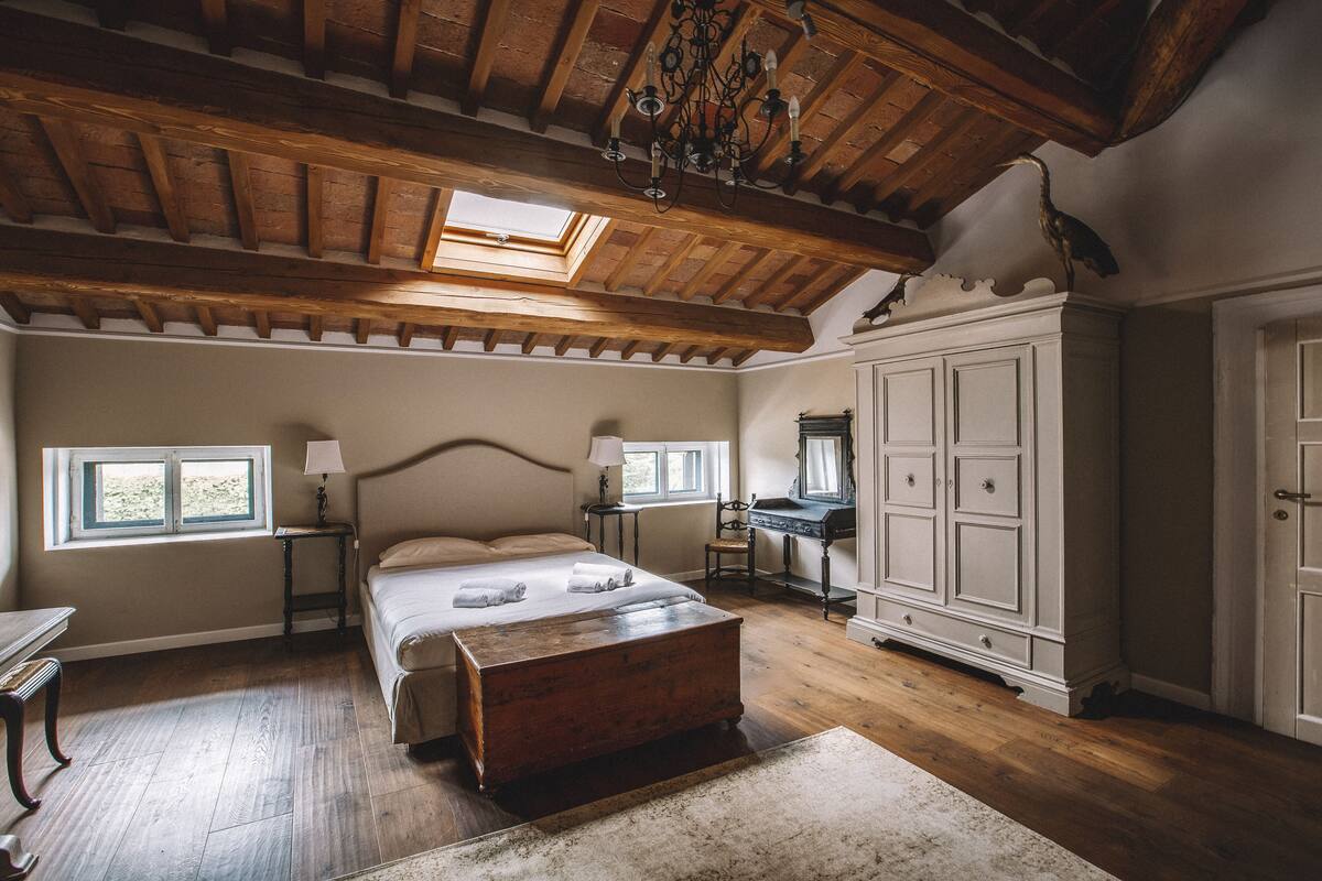 A bedroom with a wooden ceiling, a large bed, a desk, and a wardrobe.