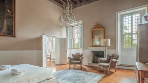 A spacious bedroom with a large bed, a chandelier, a fireplace, and a view of the outdoors through large windows. - Ludwig House (San Pietro in Cariano)