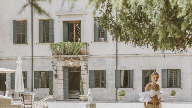 A courtyard with a building featuring a balcony with plants, a statue, and a seating area with an umbrella. - Ludwig House (San Pietro in Cariano)
