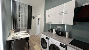 A modern kitchen with a built-in washer and dryer, a dining area with a table and chairs, and a large window with curtains. - Underfloor heating  & Free Parking in the city center (Debrecen)