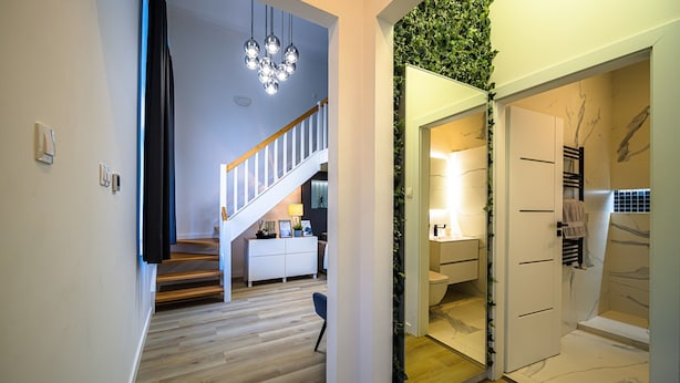 A modern interior with a staircase leading to a living area, a bathroom with a marble floor, and a green wall feature. - Underfloor heating  & Free Parking in the city center (Debrecen)