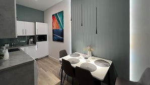 A modern kitchen with white cabinets, a microwave, and a sink. There is a dining area with a table and chairs, and a decorative painting on the wall. - Underfloor heating  & Free Parking in the city center (Debrecen)